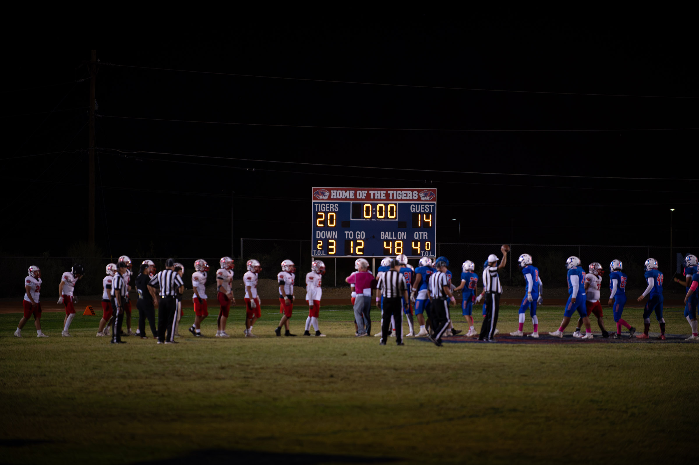 Hot Springs and Hatch Valley football players gather at midfield with the scoreboard showing the Tigers’ 20–14 victory.